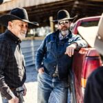 Multi-generational family of cowboys talking near rear of pickup truck-cm